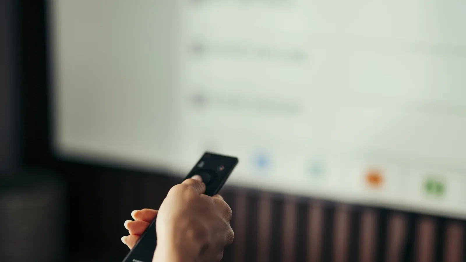 Person aiming a remote control at a television screen showing a streaming app menu