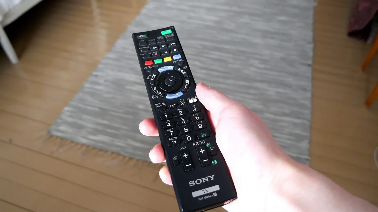 Hand holding a remote control and pointing it toward a television