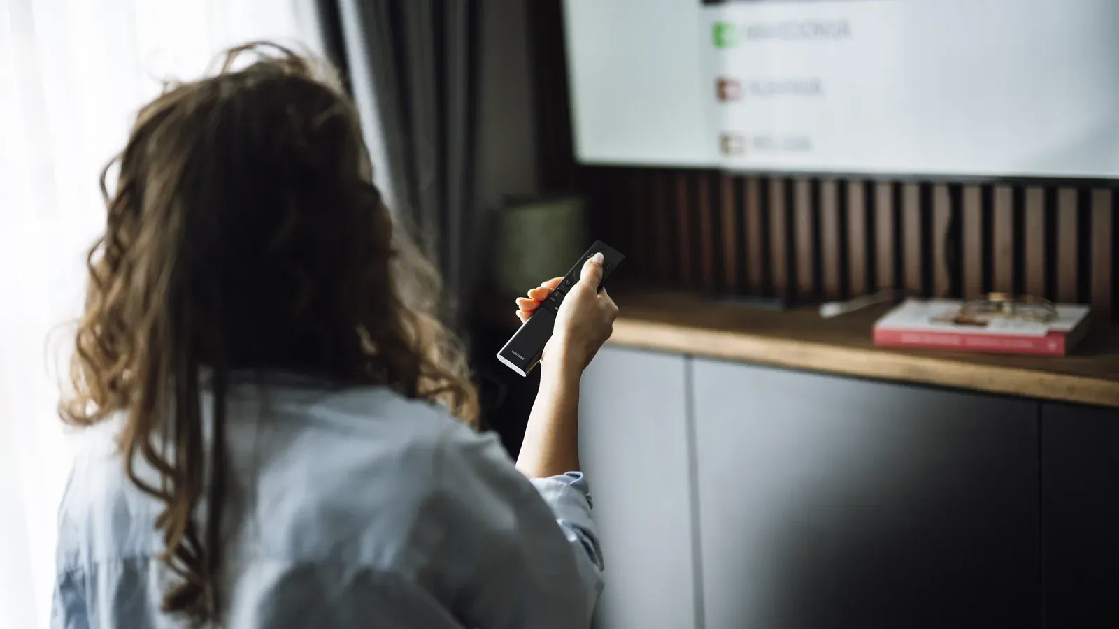 Woman pointing a remote control at a television displaying a channel list