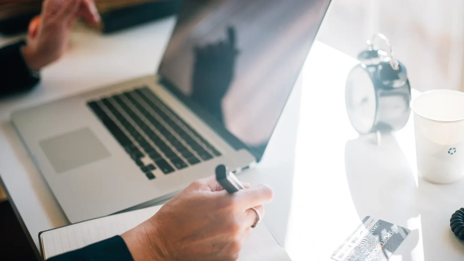 Hand typing on a laptop next to a credit card and alarm clock